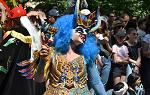 A woman taking part in the carnival of cultures parade. She is wearing a frizzy blue wig and a harlequin mask. 