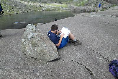 一个学生靠在一块石头上看书 